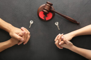 Hands of couple with keys and judge's gavel on dark background